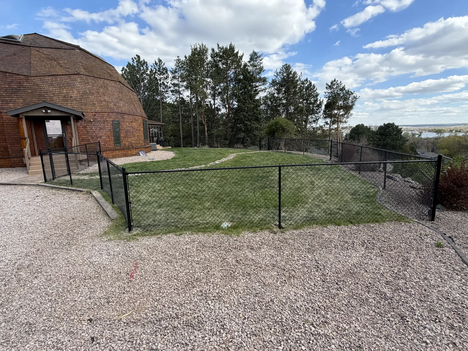 New black chain-link fence enclosing a lawn beside a wood-sided home